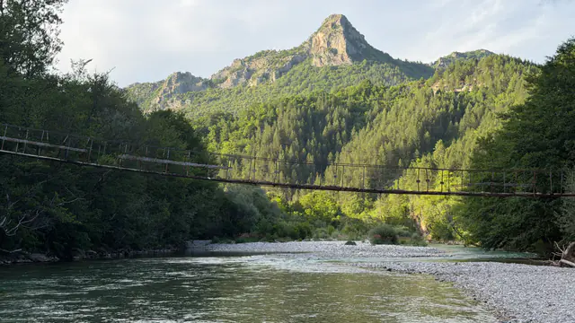 Suspension bridge over the Neretva river below mountain peaks